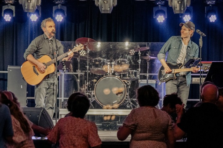Two musicians performing on stage with guitars, audience in the foreground.