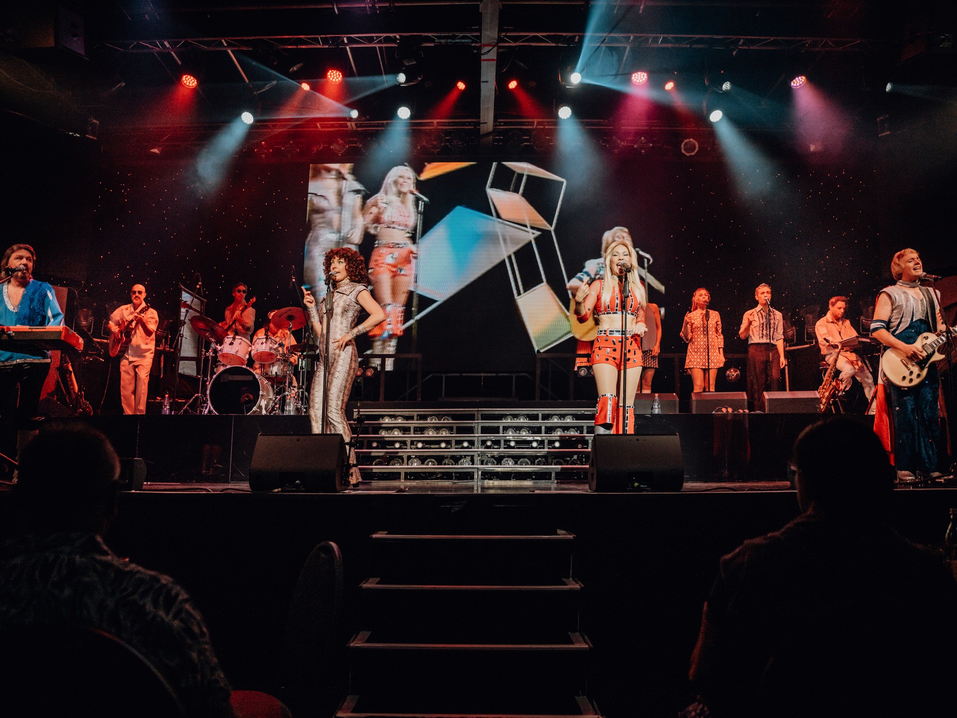 Band performing on stage with colorful outfits and light effects.