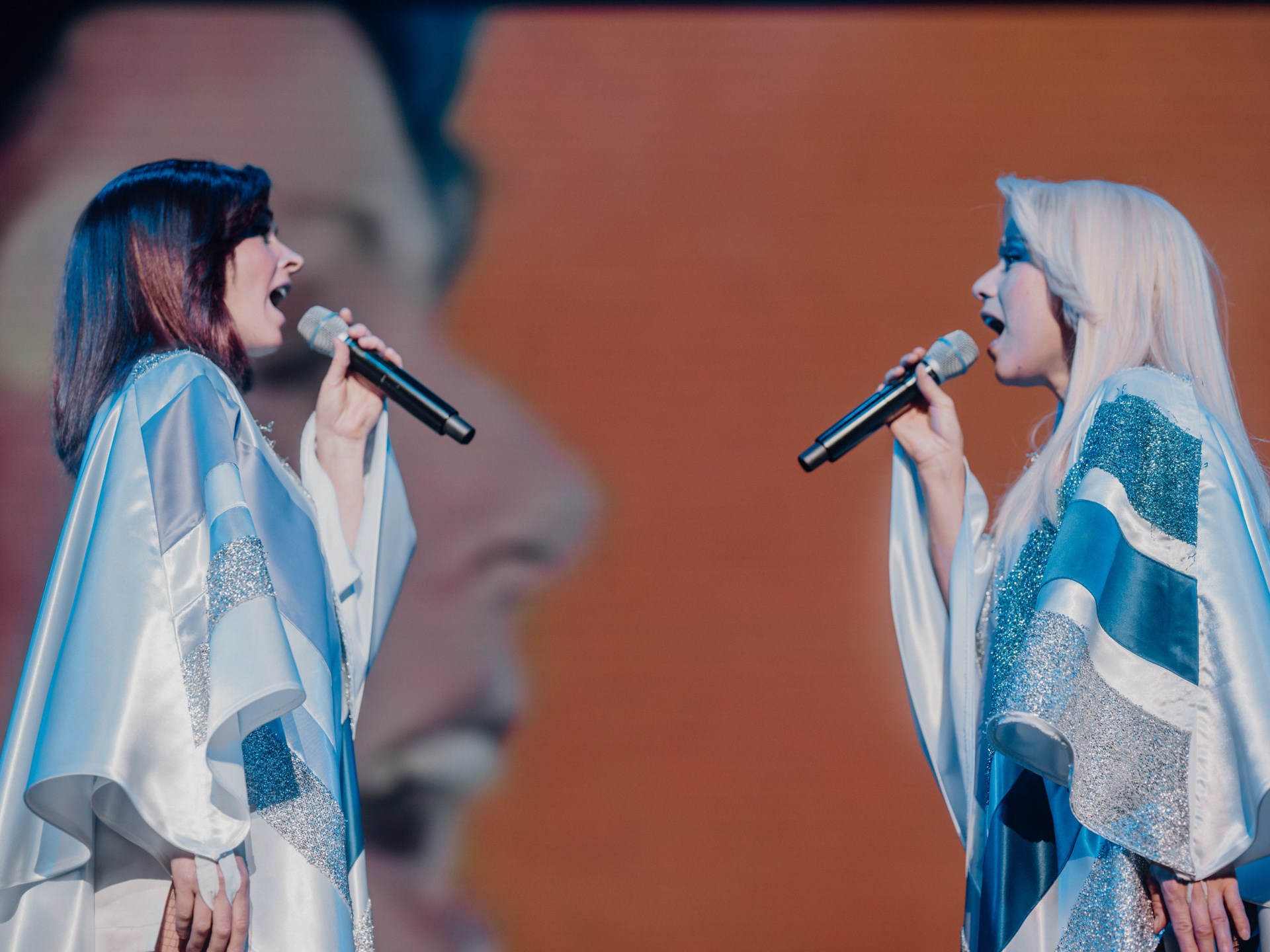 Two singers in sparkly robes performing on stage with microphones.