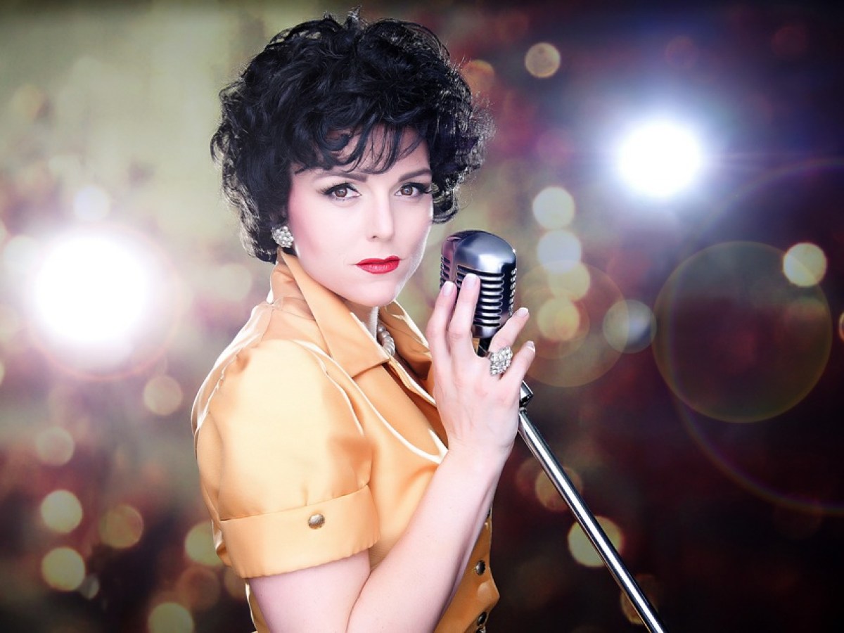 Person with vintage style holding a microphone, bokeh lights in background.
