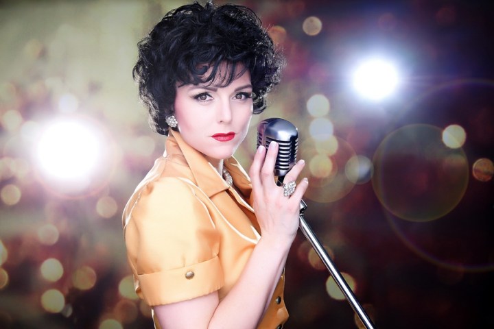 Person with vintage style holding a microphone, bokeh lights in background.