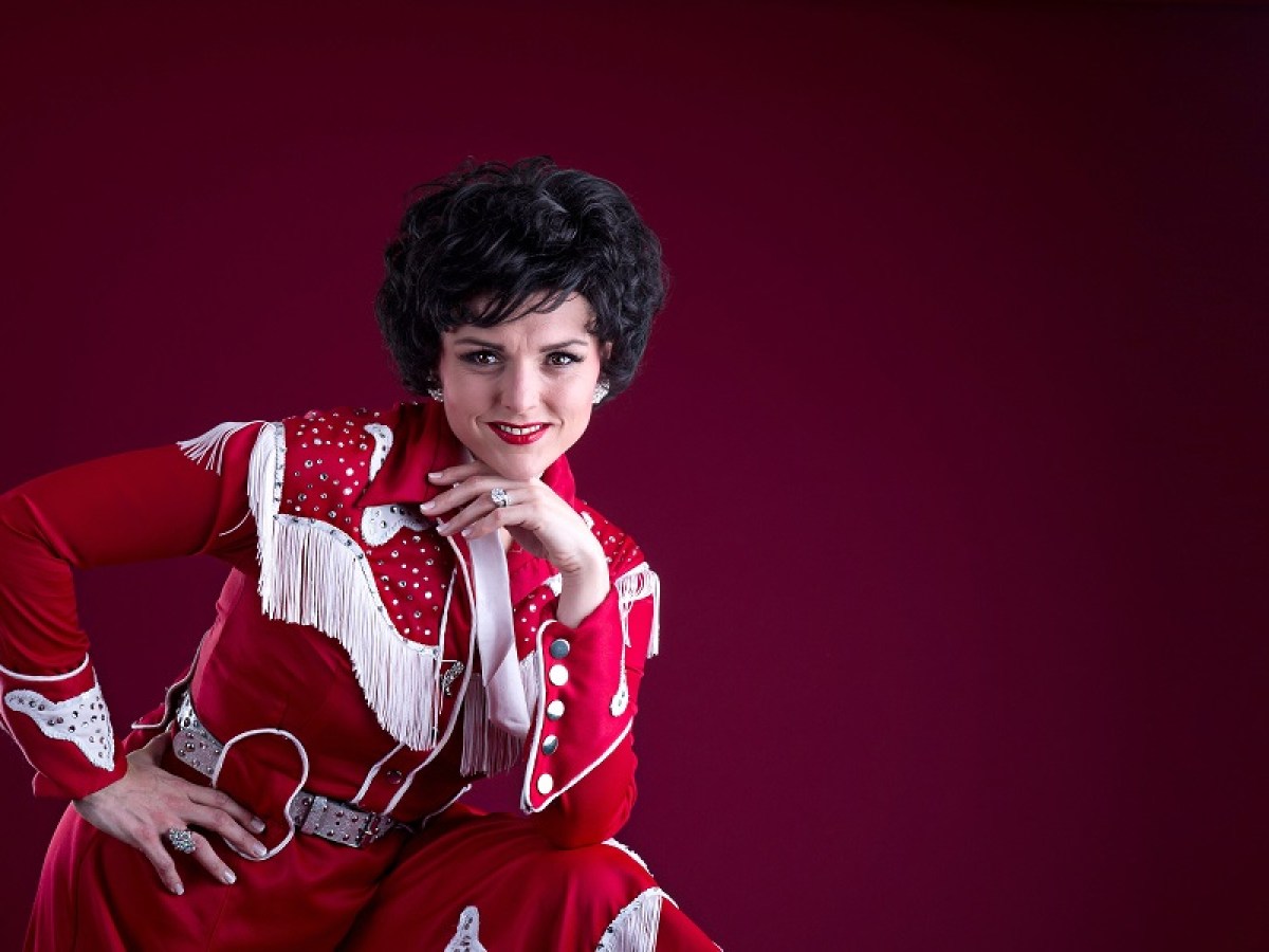 Person in red fringed outfit posing against a burgundy background.